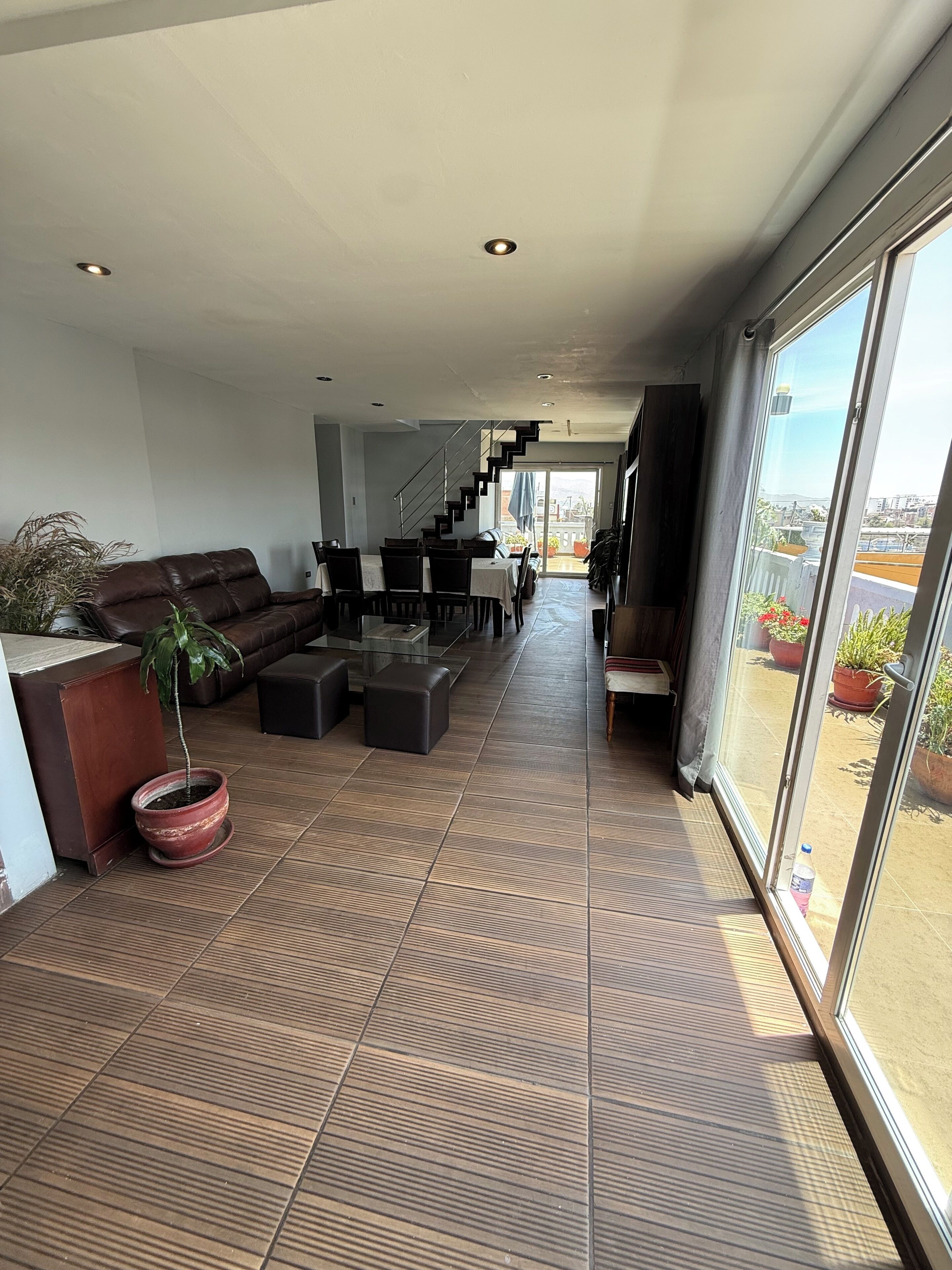 A spacious living area with a modern design, featuring a sofa, a dining table with chairs, and a staircase leading to an upper level.