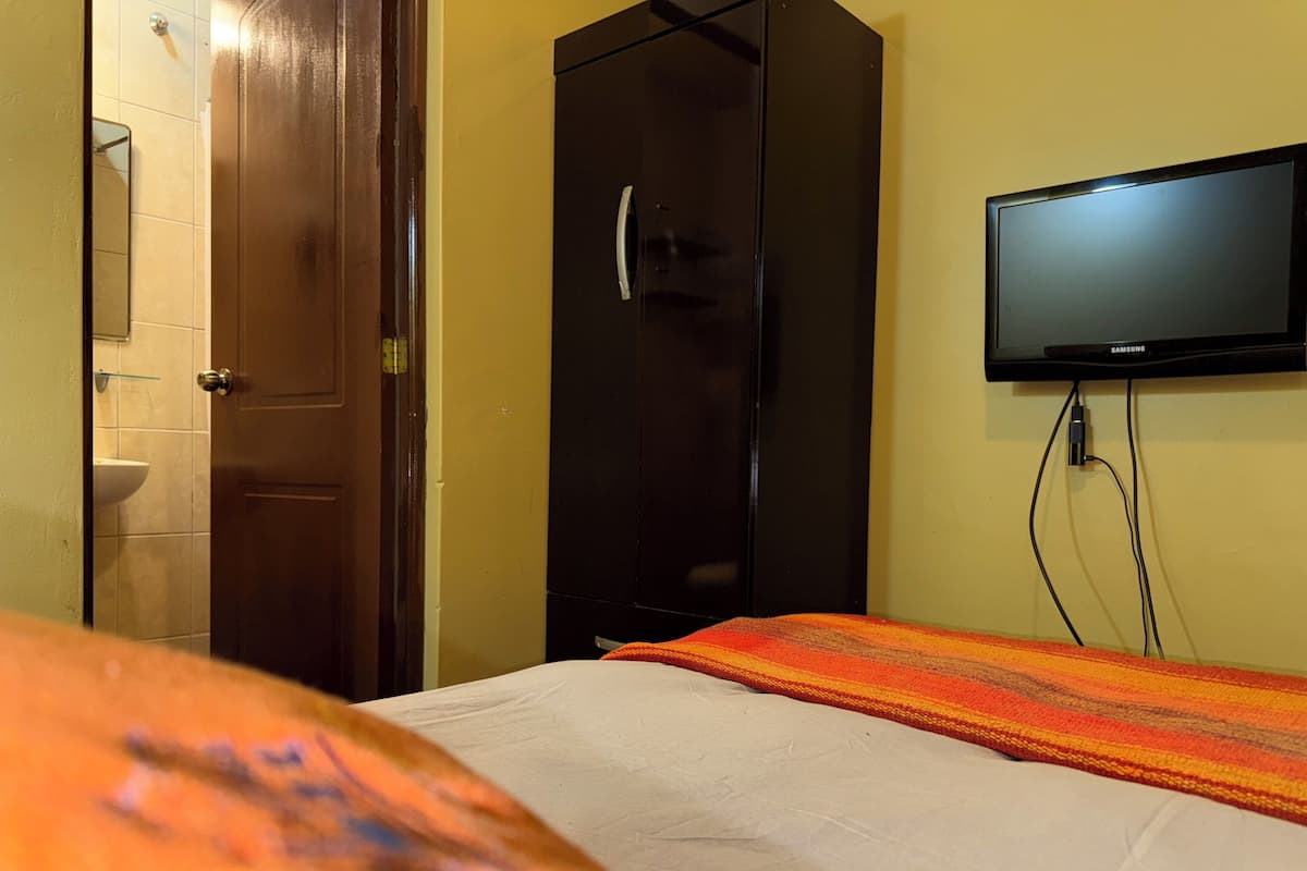 Une chambre d’hôtel équipée d’un lit, d’une armoire, d’un téléviseur fixé au mur et d’une salle de bain visible à travers une porte ouverte.