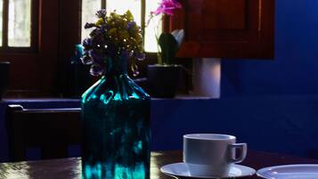 Una mesa con un jarrón azul de vidrio que contiene flores, una taza blanca y una cuchara.