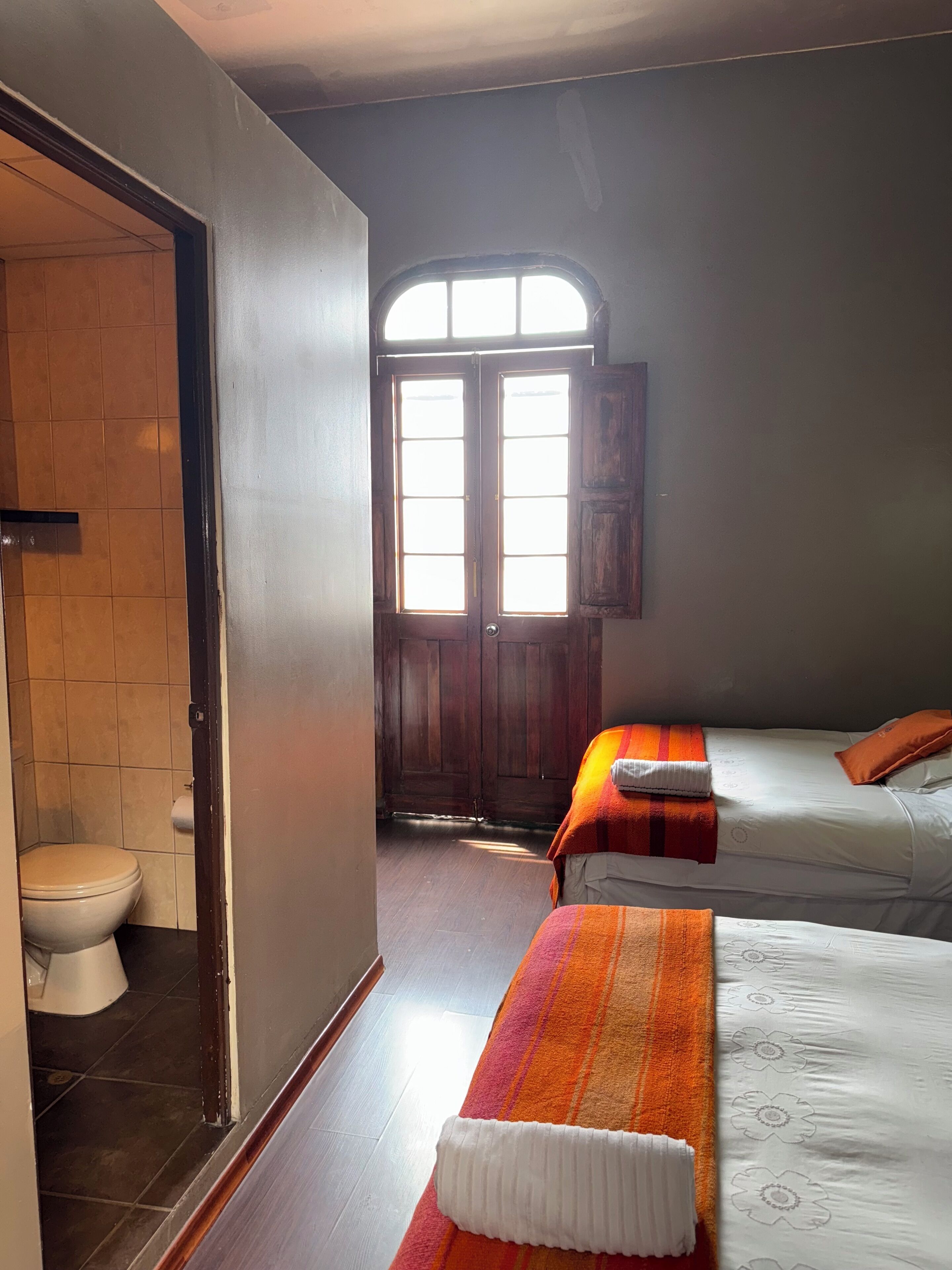 A room with a wooden door, a toilet, and two beds with colorful blankets.