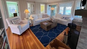 Ein modernes Wohnzimmer mit weißen Möbeln, einem blauen sechseckigen Teppich und Holzboden.