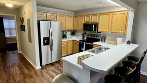 A modern kitchen with wooden cabinets, stainless steel appliances, and a central island with bar stools. - 4 Bed 4 Bath Condo Near Campus! (Auburn)