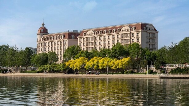 A large, historic building with a prominent dome and arched windows, situated beside a calm body of water. - The TianJin eye URcove hotel (Tianjin)
