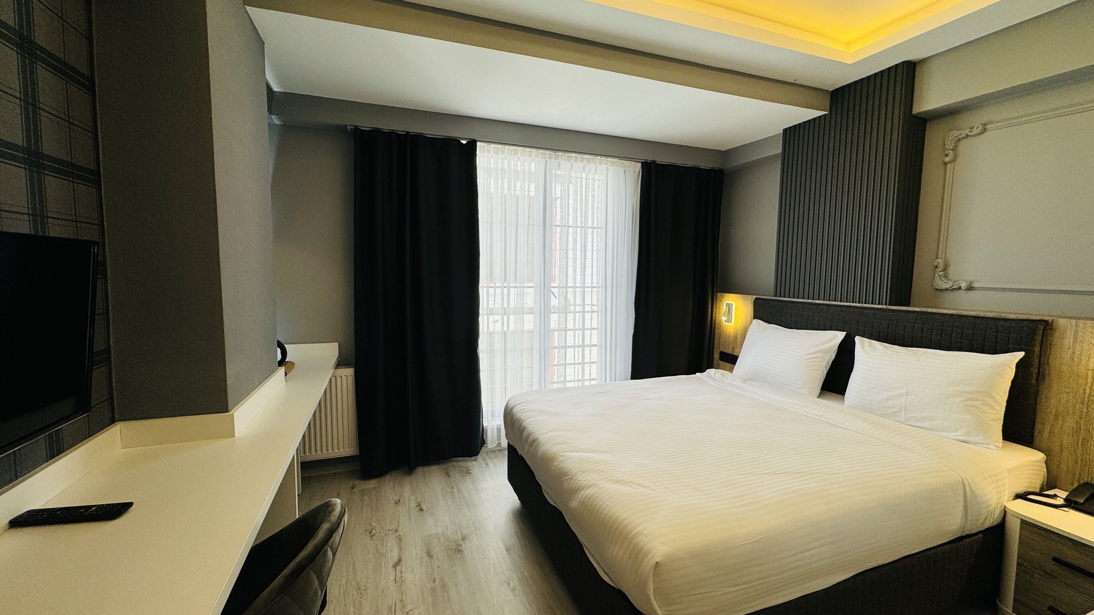 A hotel room with a bed, bedside table, lamp, and a TV on a stand.
