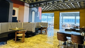 Amplio espacio interior con techo alto y una estructura de luces empotradas. Hay disposiciones para sentarse, incluyendo un largo banco y sillas individuales. El suelo está cubierto con baldosas estampadas.