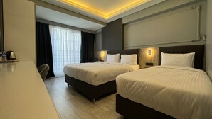 Habitación de hotel con dos camas, un escritorio y una ventana con cortinas.
