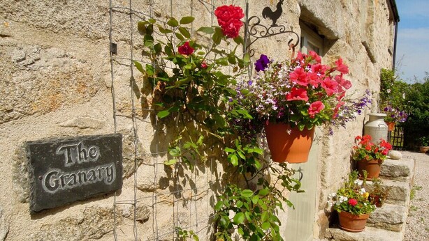A stone building with a sign reading "The Granary" and potted flowers on the wall and steps. - The Granary - Lanjeth (St Austell)