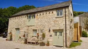 A stone building with a gravel driveway, a wooden bench, and potted plants. - The Granary - Lanjeth (St Austell)