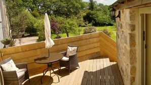 A wooden deck with a table and chairs, an umbrella, and a stone wall. - The Stables - Lanjeth (St Austell)
