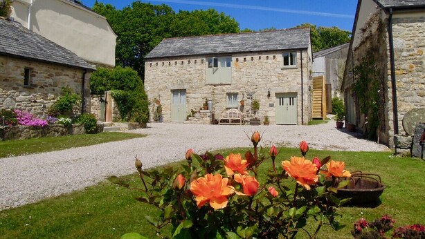 A stone building with a gravel driveway and a garden with orange flowers. - The Stables - Lanjeth (St Austell)