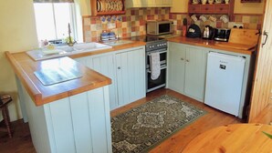 A kitchen with light blue cabinets, a microwave, a stove, a refrigerator, and a wooden countertop.