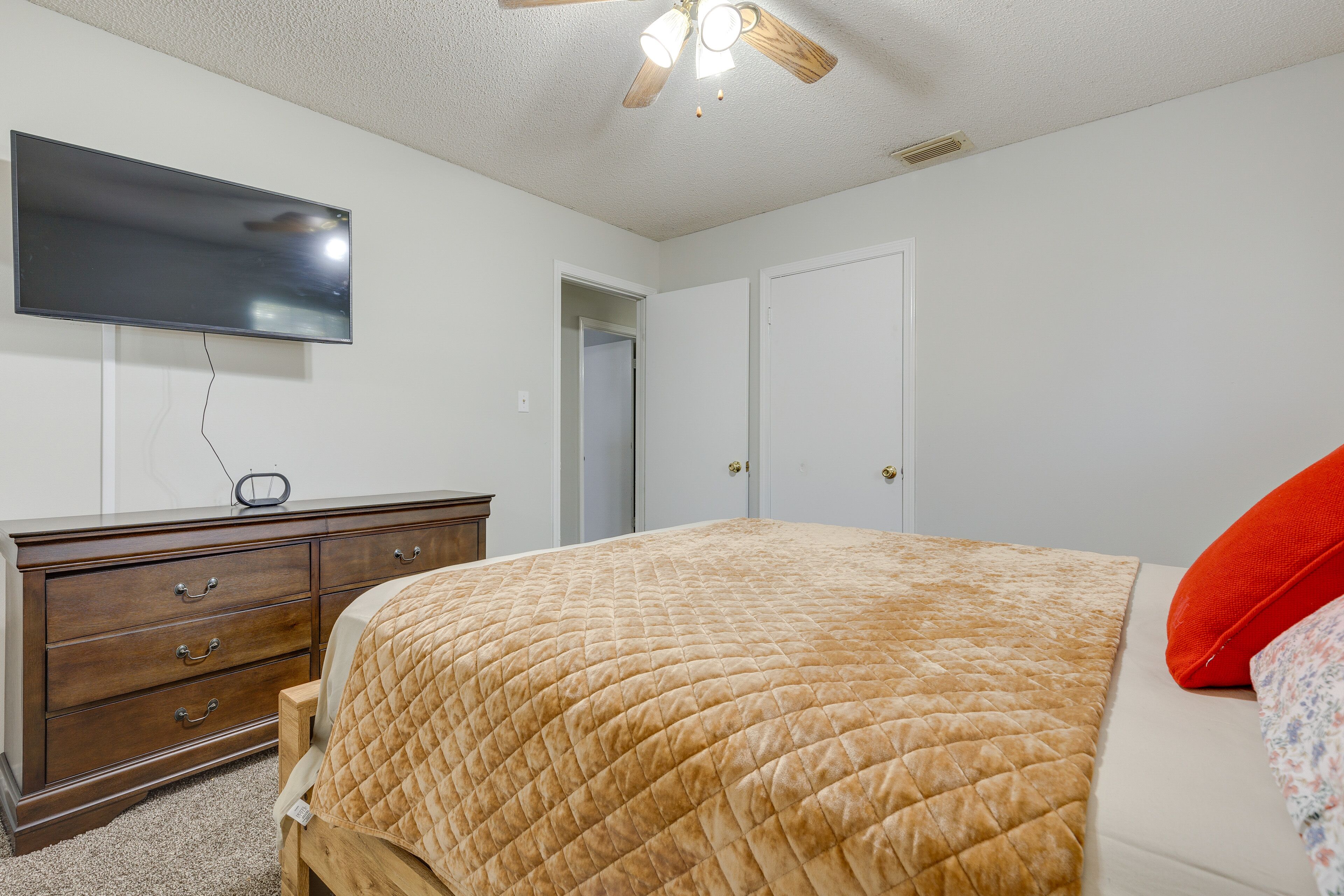 A bedroom with a bed, a dresser, a TV mounted on the wall, and a ceiling fan.