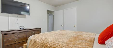 A bedroom with a bed, a dresser, a TV mounted on the wall, and a ceiling fan.