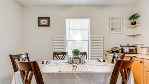 A dining area with a table set for four, surrounded by wooden chairs. A small potted plant is on the table, and there are two framed pictures on the wall. - Charming Satsuma Home ~ 14 Mi to Mobile! (Satsuma)
