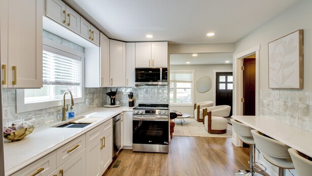 A modern kitchen with white cabinetry, stainless steel appliances, and a breakfast bar.