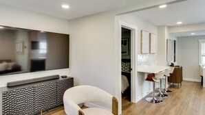 A modern living room with a flat-screen TV, a sofa, and a dining area with a table and chairs.