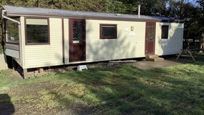 A small, single-story mobile home with a front porch, a small attached garage, and a fenced yard. - Park Lodge sleeps 6 On Beautiful Rural Welsh Farm (Builth Wells)