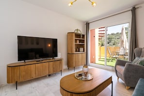 Een moderne woonkamer met een flatscreen televisie, houten meubels en uitzicht door een glazen deur op een buitenruimte.
