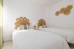 Een kamer met twee bedden, elk met een rieten hoofdbord, witte beddengoed en een klein nachtkastje met een lamp.