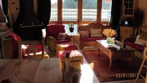 A cozy living room with a fireplace, wooden furniture, and large windows. - Appartement Camille Bonaventure (Les Contamines-Montjoie)