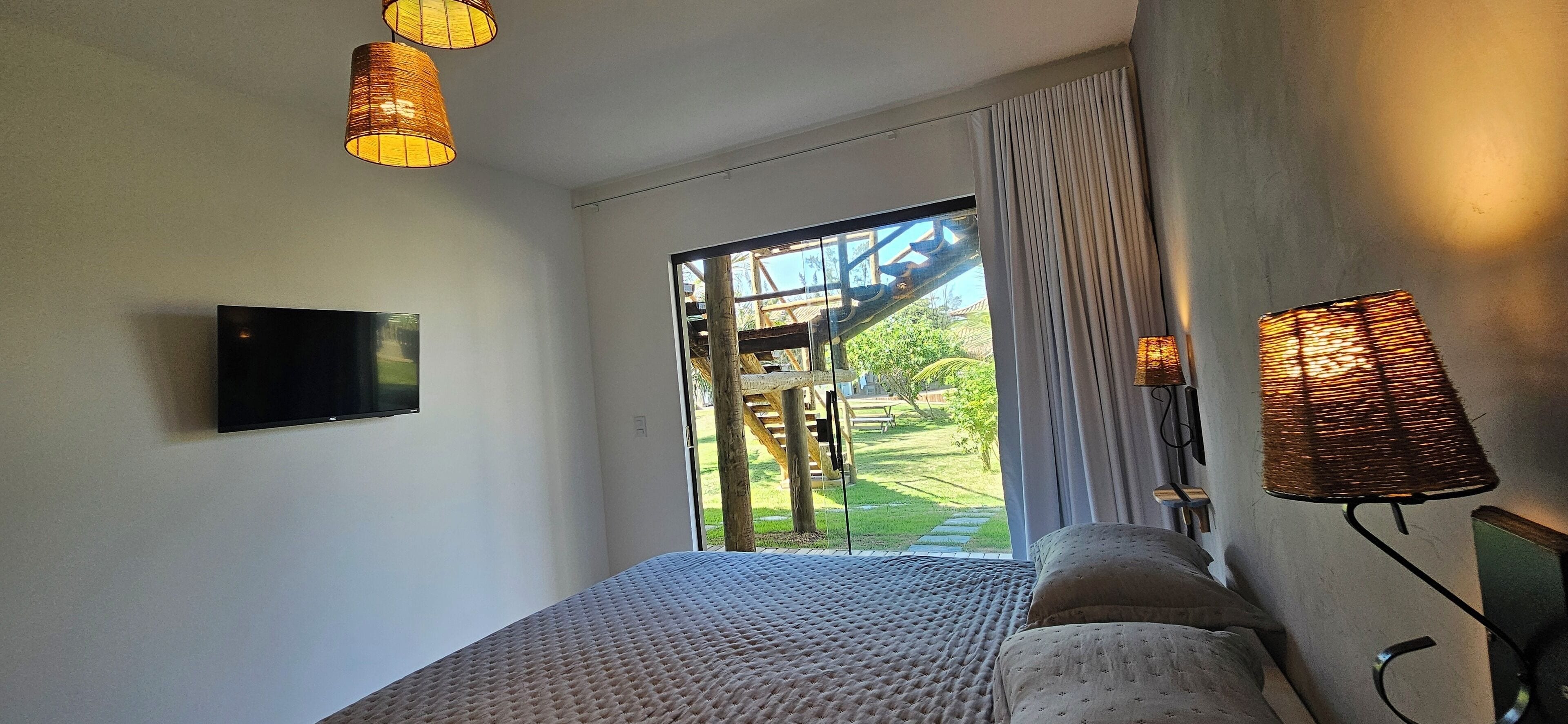 Un dormitorio con cama, televisión y vista a un jardín por una puerta de cristal.