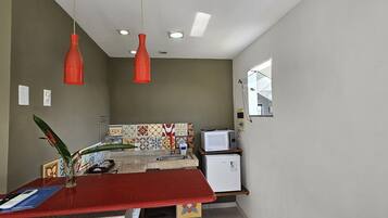 A compact kitchen with a red countertop, a microwave, a refrigerator, and a window with a view.