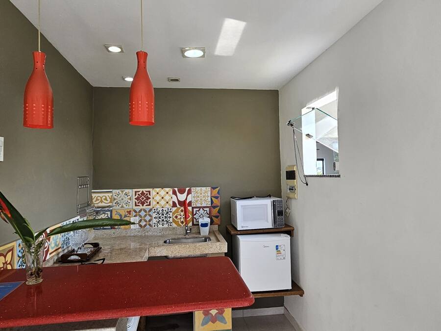 A compact kitchen with a red countertop, a microwave, a refrigerator, and a window with a view.