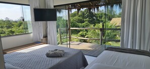 A bedroom with a large window, a bed, a TV, and a balcony with a view of the forest. - Kite Nomade (Arraial do Cabo)