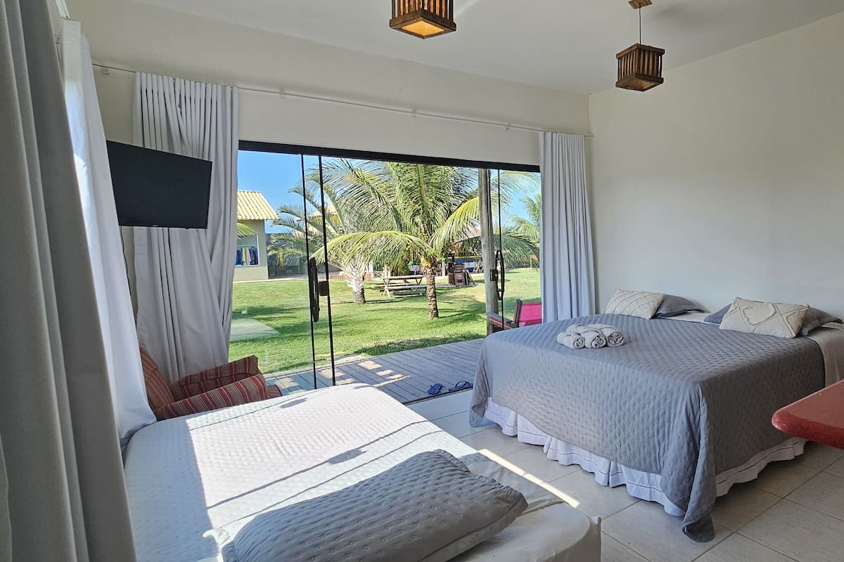 A bedroom with two beds, a TV, a desk, and a view of a garden.