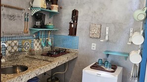 A compact kitchen with a granite countertop, a refrigerator, and a hanging light fixture. - Kite Nomade (Arraial do Cabo)