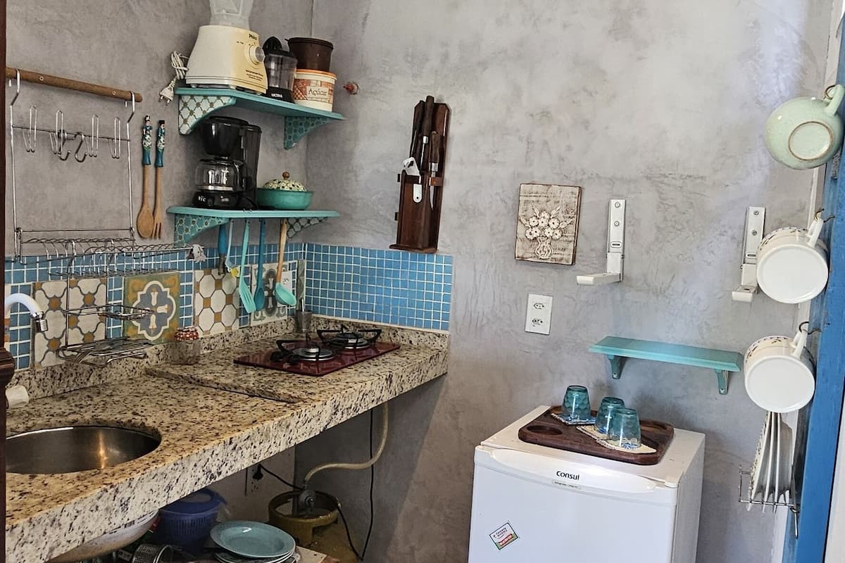 A compact kitchen with a granite countertop, a refrigerator, and a hanging light fixture.