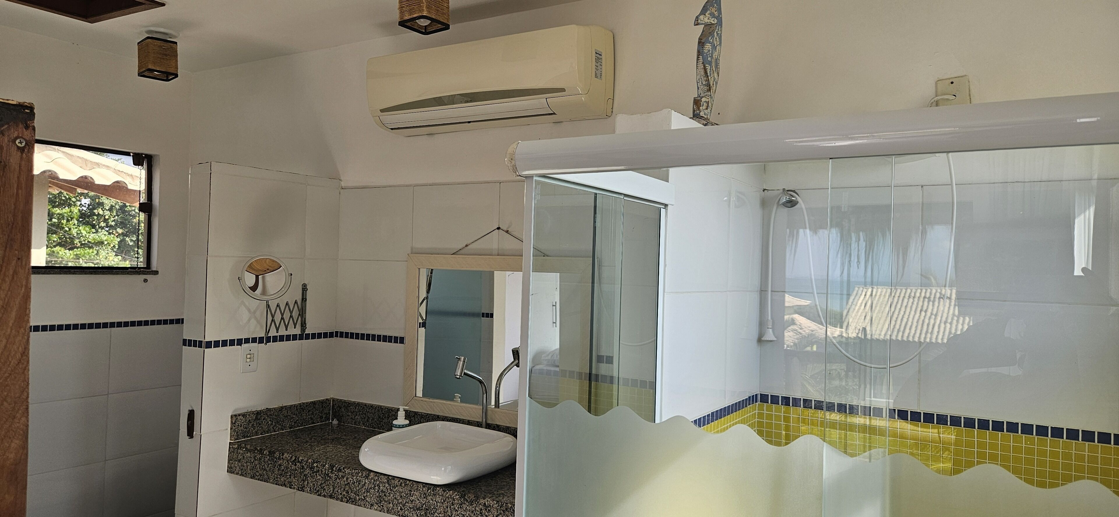 Casa de banho com lavatório, espelho, chuveiro e unidade de ar condicionado.