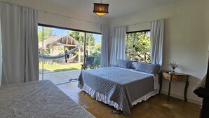 A bedroom with two beds, large windows, a hammock outside, and a small table with a plant. - Kite Nomade (Arraial do Cabo)