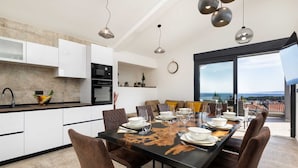 Une cuisine moderne avec des meubles blancs, un plan de travail noir et un coin repas doté d’une grande table pouvant accueillir six personnes.