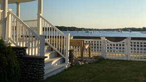 A waterfront property with a stone staircase leading to a white porch, a wooden deck, and a view of boats on the water. - BELLE of the BEACH: 30 ft to gorgeous PRIVATE BEACHFRONT home SLEEPS up to 13 (Wareham)