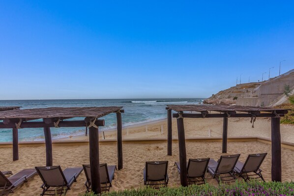 Una playa con pérgolas de madera y sillas de descanso frente al océano.