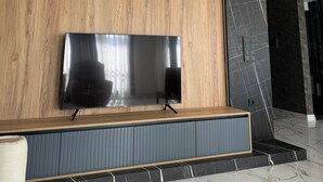 A modern living room with a large flat-screen TV mounted on a wooden panel wall, a dark marble accent wall, and a marble-tiled floor. - Villa mit Privatem Pool in der Nähe von Strand und Einkaufszentrum (Kuşadası)