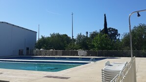 Piscina com deck de concreto, cerca de metal e uma árvore alta ao fundo.
