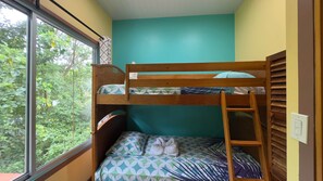A bunk bed room with a window, a teal wall, and a wooden ladder.