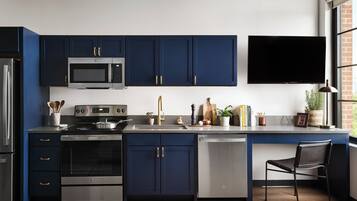 Uma cozinha moderna com armários azul-escuros, eletrodomésticos de aço inoxidável e uma TV de tela plana montada acima do balcão.
