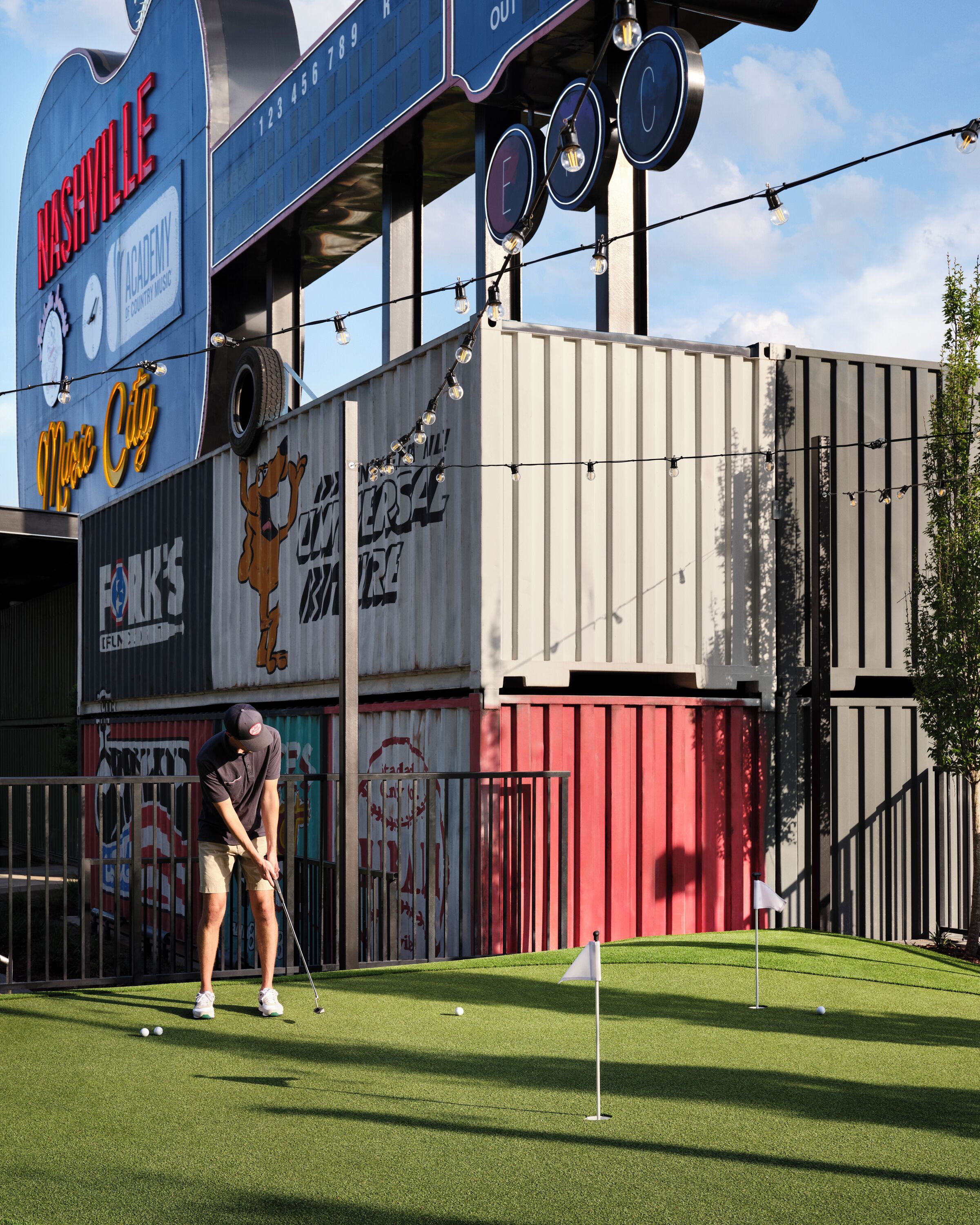 A golf course with a person playing, a building with 'Nashville' and 'Music City' signage, and a mural of a dog.