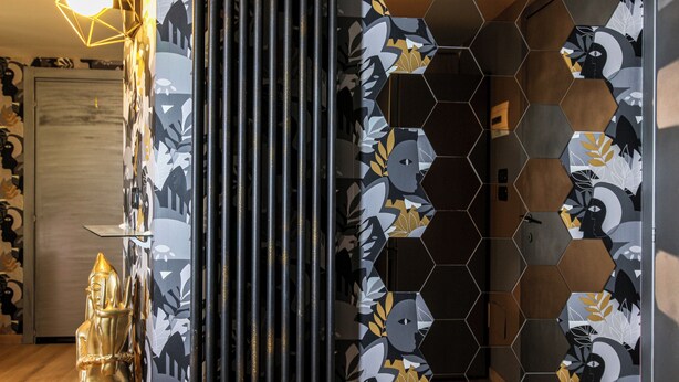 A hallway with patterned wallpaper, a decorative golden figure, and hexagonal wall tiles. - Flytosuite aeroporto attico mansarda  (Calderara di Reno)