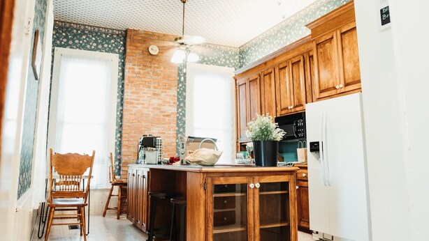 Une cuisine avec des armoires en bois, un mur d’accent en briques, un îlot central en bois et un ventilateur de plafond.