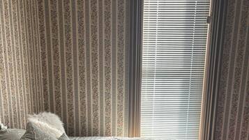 A bedroom with a bed, pillows, a window with blinds, and striped wallpaper.