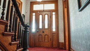 Un escalier en bois, recouvert d’un tapis rouge, mène à une grande porte en bois à plusieurs panneaux, ornée d’une vitre.