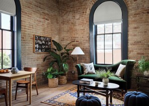 Una habitación acogedora con pared de ladrillo, un sofá verde, una mesa con lámpara y un ventanal grande.