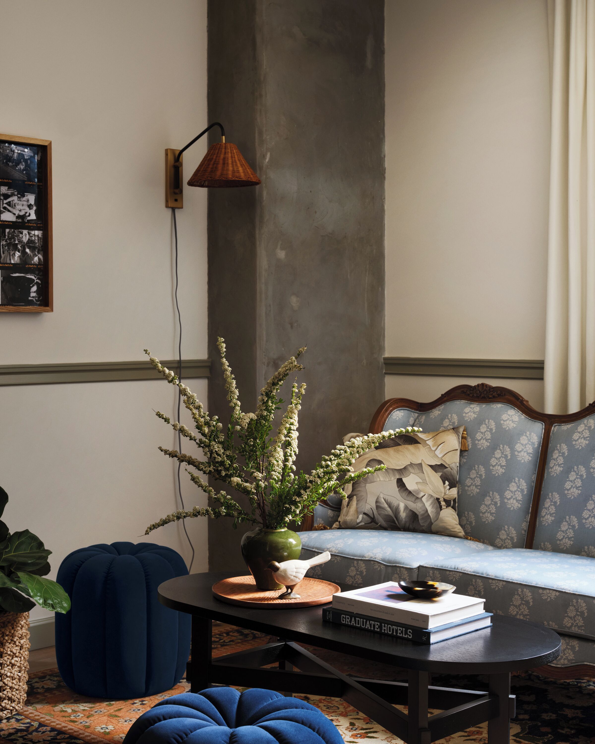 Ein Wohnzimmer mit einer Couch, einem Couchtisch mit einem Buch, einer Vase mit Blumen, einer Lampe und einem gerahmten Bild an der Wand.