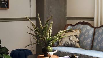 Ein Wohnzimmer mit einer Couch, einem Couchtisch mit einem Buch, einer Vase mit Blumen, einer Lampe und einem gerahmten Bild an der Wand.