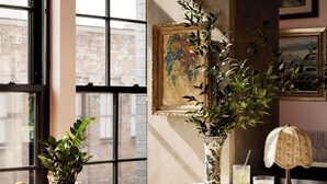 Un coin bar avec une grande fenêtre, une plante en pot, un saladier rempli d’agrumes, un verre de bière et une lampe décorative.