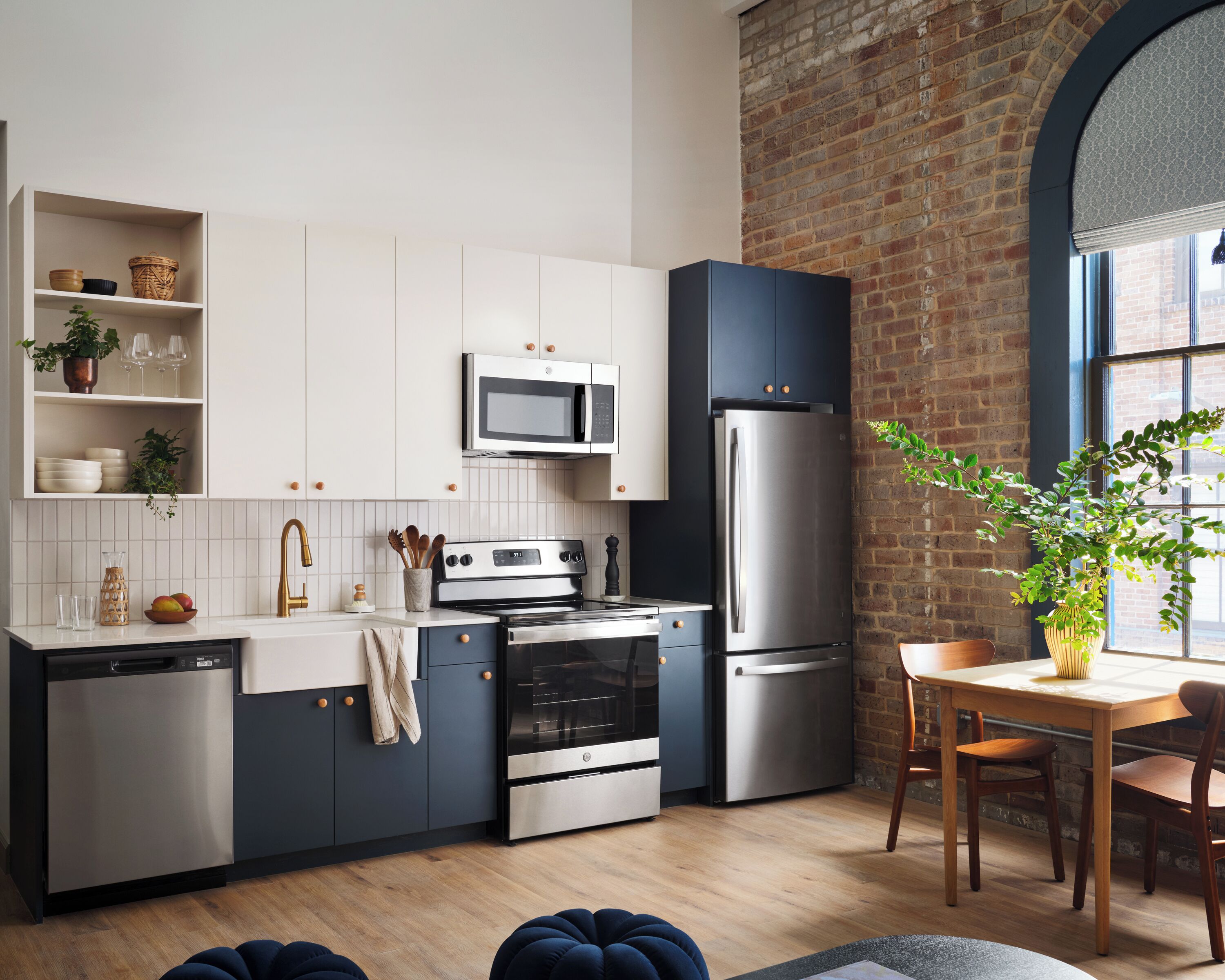 Een moderne keuken met witte kasten, roestvrijstalen apparatuur, een bakstenen muur en een eethoek met houten meubels.